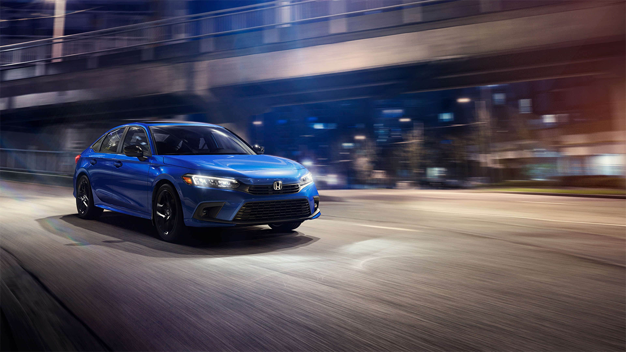 3/4 front view of blue Civic Sedan driving off a city offramp at night.
