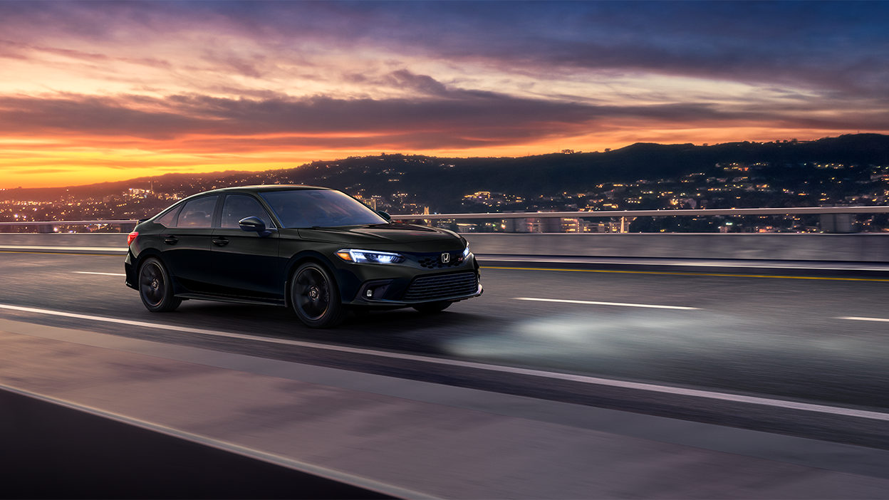 3/4 front sideview of black Civic Si driving on a highway at dusk. 