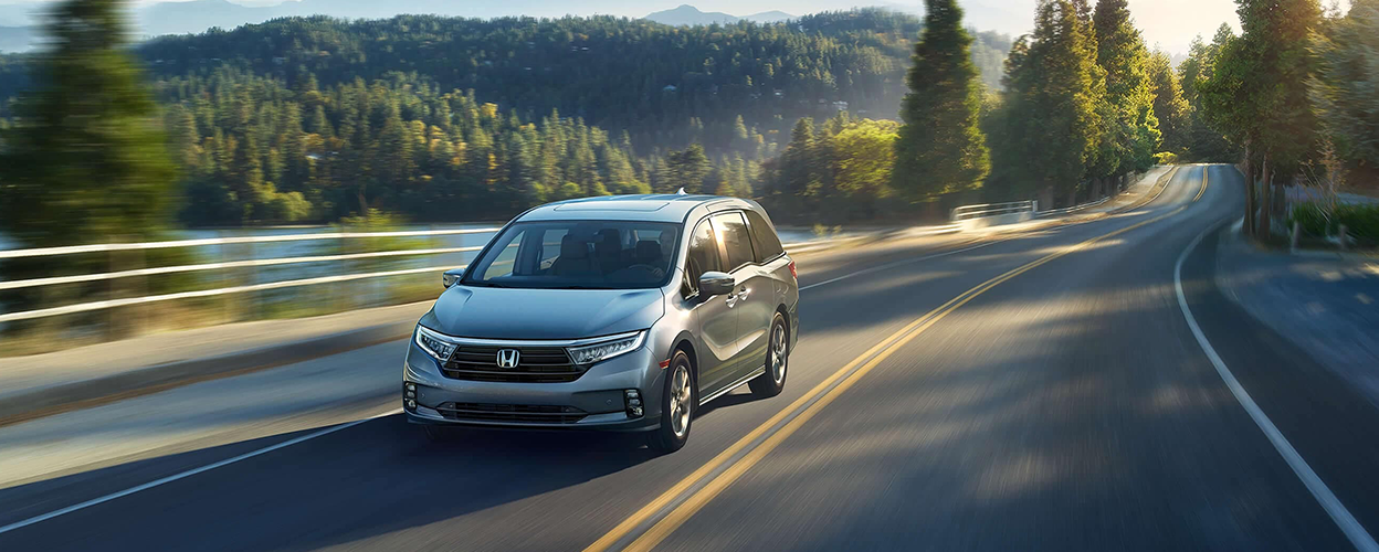 3/4 front view of grey Odyssey driving on lakeside road.