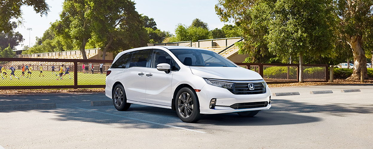 3/4 front view of white Odyssey parked near a soccer field.
