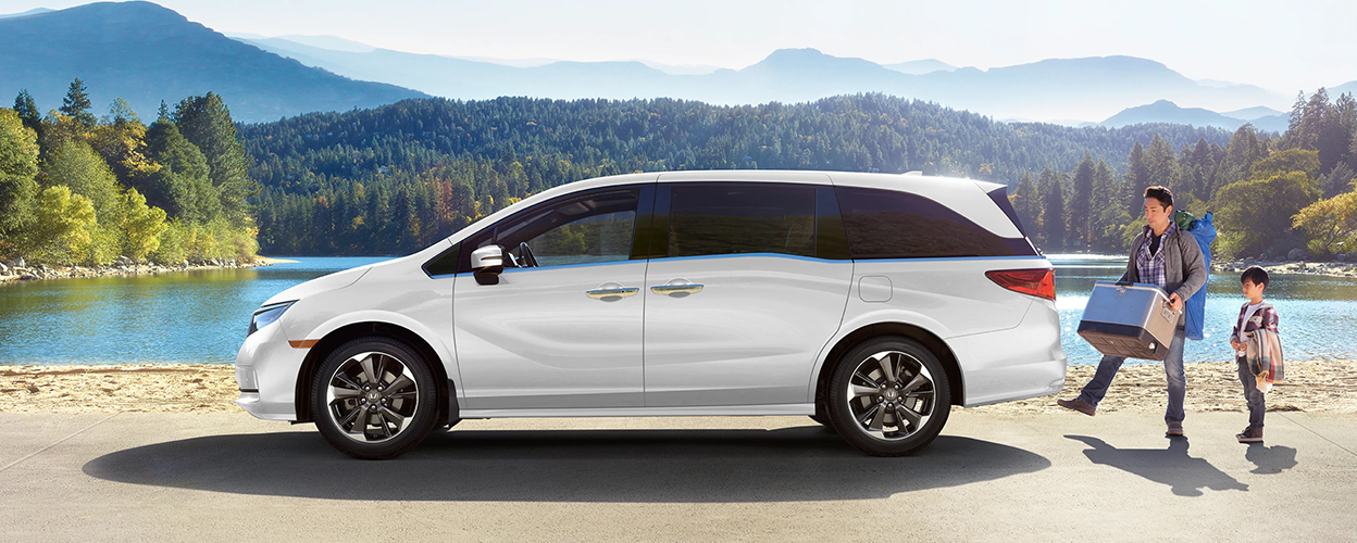 Sideview of white Odyssey, parked lakeside. Dad and kid loading up the trunk.