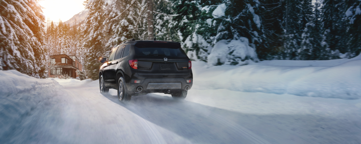 3/4 rear view of black Passport driving on snowy forest road.